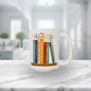 White 15 oz mug with seven books on a shelf with wildflowers for bookmarks. Book titles can be customized to a person's favorite books.
