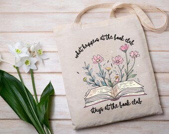 May include: A white tote bag with a floral design and the text "what happens at the book club stays at the book club".