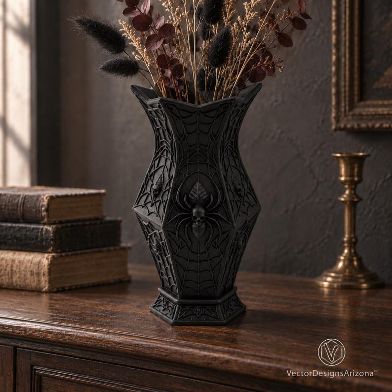 Arachvelle matte-black gothic spiderweb skull vase with dried botanicals on a dark walnut console.