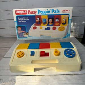 以下が含まれることがあります： ヴィンテージのPlayskool Busy Poppin' Palsディズニーキャラクターおもちゃ。おもちゃは、カラフルなブロックとインタラクティブな要素を備えたクリーム色のベースが特徴です。箱には、飛び出すディズニーのキャラクターが描かれています。箱のテキストは「A surprise box of sight, sound and action」と書かれています。