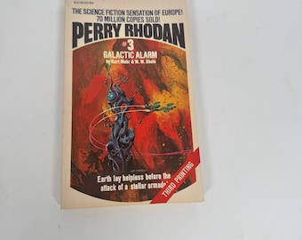 May include: A vintage paperback book titled "Perry Rhodan #3 Galactic Alarm." The cover features a vibrant illustration of a science fiction scene with a dark blue alien figure and a green spaceship against a red and orange background. The text reads "Third Printing."