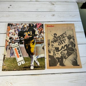 Op de afbeelding: Twee vintage Purdue Boilermakers voetbalwedstrijdprogramma's. Eén programma toont een speler in een zwart-gouden uniform die met de bal rent. Het andere programma heeft de woorden "Roses are Black" met een menigte mensen.