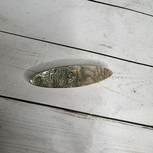 Op de afbeelding: Ovale haarclip met een iriserend abalone schelpontwerp. De clip heeft een mix van groene, zilveren en roze tinten, waardoor het een uniek accessoire is. De clip is ongeveer 10 cm lang.