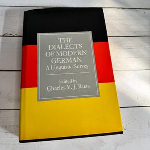 Könnte beinhalten: Ein Buch mit dem Titel "The Dialects of Modern German: A Linguistic Survey", herausgegeben von Charles V. J. Russ. Das Cover zeigt die Farben der deutschen Flagge: Schwarz, Rot und Gelb. Der Titel befindet sich in einem grauen Feld.