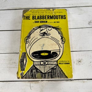 May include: A vintage hardcover book titled The Blabbermouths by Dan Sorkin as told to Joe Price, with an introduction by Shelley Berman. The yellow cover features a black line drawing of a person with a large open mouth containing a vinyl record.