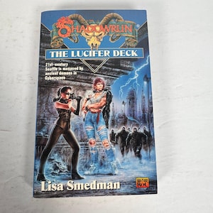 May include: A paperback book titled "Shadowrun: The Lucifer Deck" by Lisa Smedman. The cover art features two figures in a futuristic setting with a cityscape and lightning. The book's cover is predominantly blue.