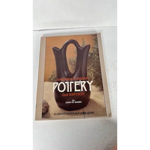 May include: A book titled "American Indian Pottery 2nd Edition" with a brown cover. The cover features a dark brown pottery vase against a backdrop of sand and greenery. The book is an identification and value guide.