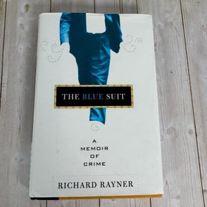 May include: A hardback book titled "The Blue Suit" with a white cover. The cover features a blue suit illustration and the text "A Memoir of Crime" and the author's name, Richard Rayner.