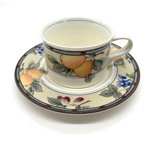 Könnte beinhalten: Cremefarbenes Tee-Set mit einem Fruchtdesign. Die Tasse und die Untertasse weisen ein sich wiederholendes Muster aus Orangen, Trauben und Blättern auf. Der Rand der Tasse und der Untertasse ist mit einem blauen und braunen Rand versehen.