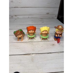 May include: Four vintage Little People figures. One figure is crawling, three are sitting in green inner tubes. One figure has brown hair and a green headband, two have orange and yellow hair, and one is wearing a cowboy hat and riding a red tricycle.