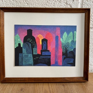 May include: A framed print of a colorful abstract painting depicting a graveyard at sunset. The painting features a variety of tombstones and a tall, slender structure in the background. The colors are vibrant and bold, with shades of purple, pink, orange, and green.