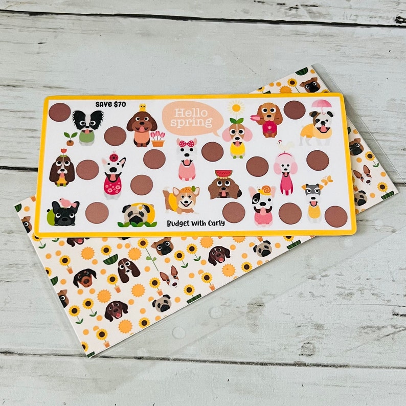 May include: A yellow and white card with a dog-themed spring budget tracker. The card has a title that says "Hello Spring" and "Budget with Carly". The card has a variety of dog illustrations with different spring-themed accessories. The card has a "Save $70" label.