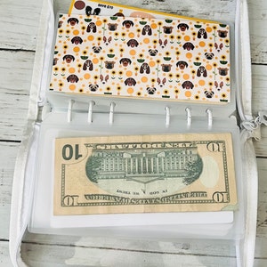 May include: A white zippered pouch with a clear plastic window. The pouch contains a $10 bill and a card with a pattern of dogs and sunflowers. The card also has the text "Save $70".