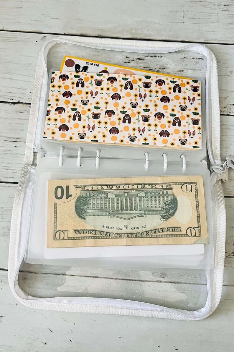 May include: A white zippered pouch with a clear plastic window. The pouch contains a $10 bill and a card with a pattern of dogs and sunflowers. The card also has the text "Save $70".