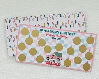 May include: A pink and blue Christmas savings challenge card with a chequered background. The card has gold baubles and the text "HAVE A GROOVY CHRISTMAS savings challenge SAVE £100" and "TIS THE SEASON".