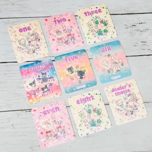 Pode incluir: Um conjunto de nove cartões retangulares com ilustrações de desenhos animados e os números de um a oito, mais "dealer's choice". Cada cartão apresenta um design diferente e uma combinação de cores pastel, sobre um fundo de madeira clara.