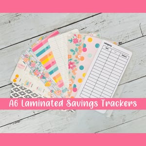May include: A6 size laminated savings trackers with various colorful designs, including floral, geometric, and polka dot patterns. The trackers have a section for category, date, and balance.