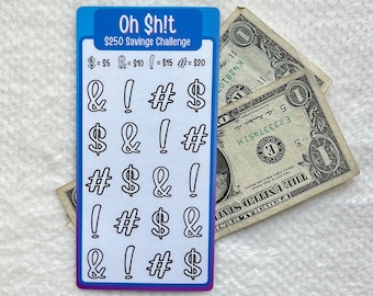 May include: A white card with the text "Oh $h!t $250 Savings Challenge" and a grid of symbols: dollar signs, ampersands, exclamation points, and number signs. The symbols are arranged in a grid of five rows and four columns. The card is on a white surface.
