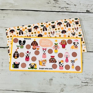 May include: A yellow and brown card with a dog-themed design. The card has a circle for each day of the month and features cute illustrations of dogs in various outfits. The text "Hello spring" is in a speech bubble and the text "Save $70" and "Budget with Carly" are also on the card.
