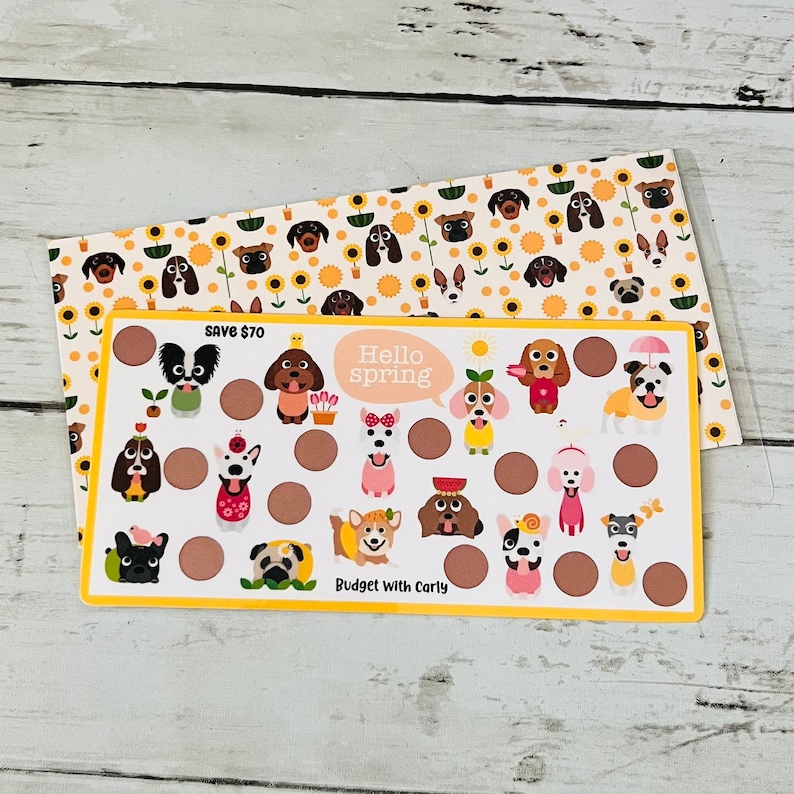 May include: A yellow and brown card with a dog-themed design. The card has a circle for each day of the month and features cute illustrations of dogs in various outfits. The text "Hello spring" is in a speech bubble and the text "Save $70" and "Budget with Carly" are also on the card.