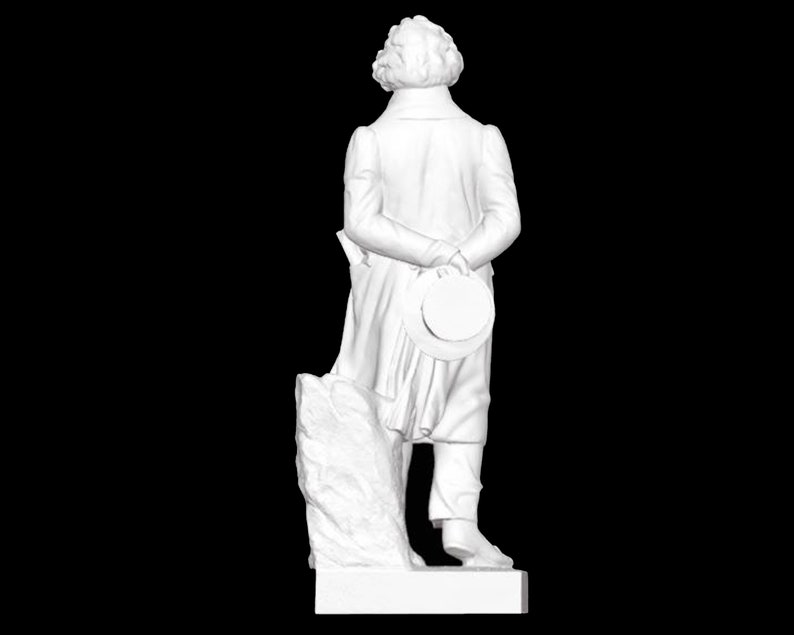 May include: White marble statue of a man standing on a plinth. The man is wearing a long coat and has his hands behind his back. He is holding a hat in his right hand.