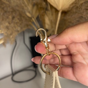 May include: A cream-colored strap with a gold-toned metal clasp and ring.
