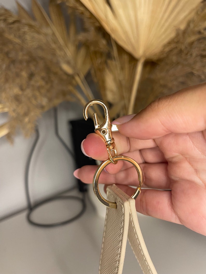 May include: A cream-colored strap with a gold-toned metal clasp and ring.