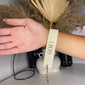 May include: A white leather keychain with a gold metal clasp and the name "SOFI" written in gold lettering.