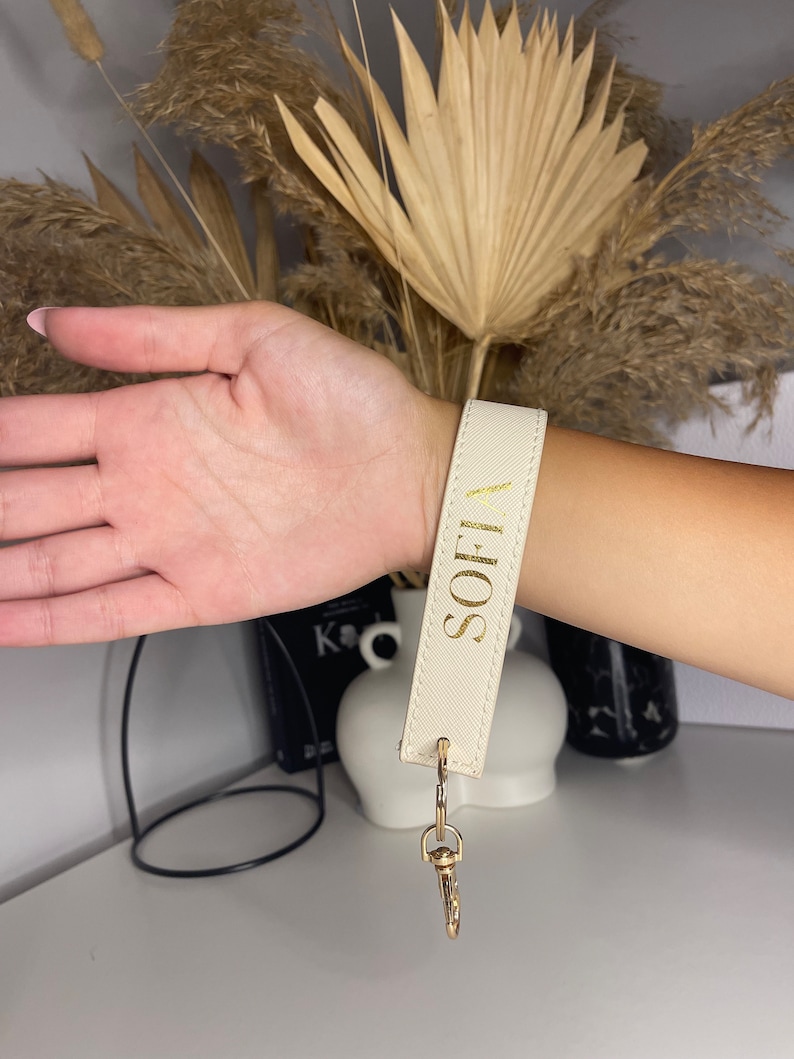May include: A white leather keychain with a gold metal clasp and the name "SOFI" written in gold lettering.