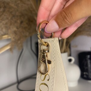 May include: A white keychain with a gold metal clasp and the name "SOPH" written in gold lettering.