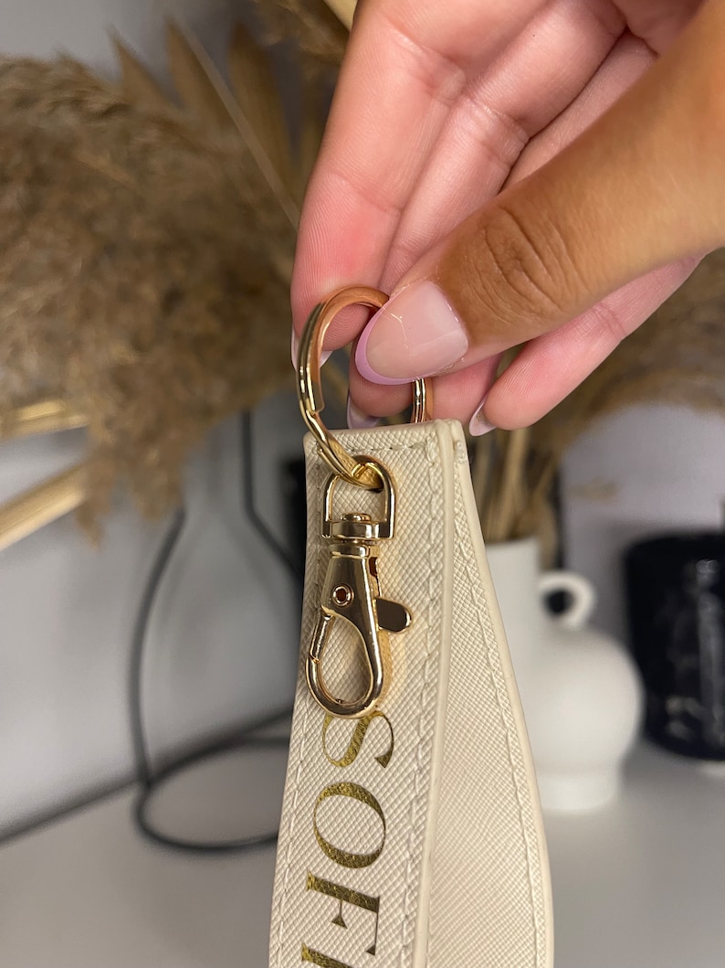 May include: A white keychain with a gold metal clasp and the name "SOPH" written in gold lettering.