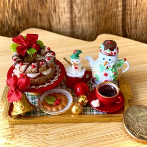 Peut inclure: Une miniature sur le thème de Noël sur un plateau doré comprenant une couronne de pâtisserie avec un nœud rouge, une figurine de bonhomme de neige dans une tasse rouge, une théière bonhomme de neige, une tartelette, une tasse rouge et une pièce de 10 centavos.