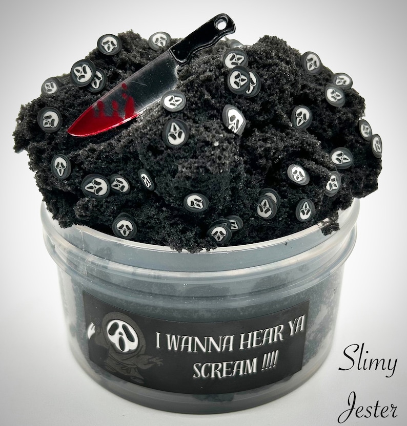 May include: Black slime with white ghost face charms and a red-handled knife. The slime is in a clear plastic container with a black label that reads "I wanna hear ya scream!!!" and "Slimy Jester".