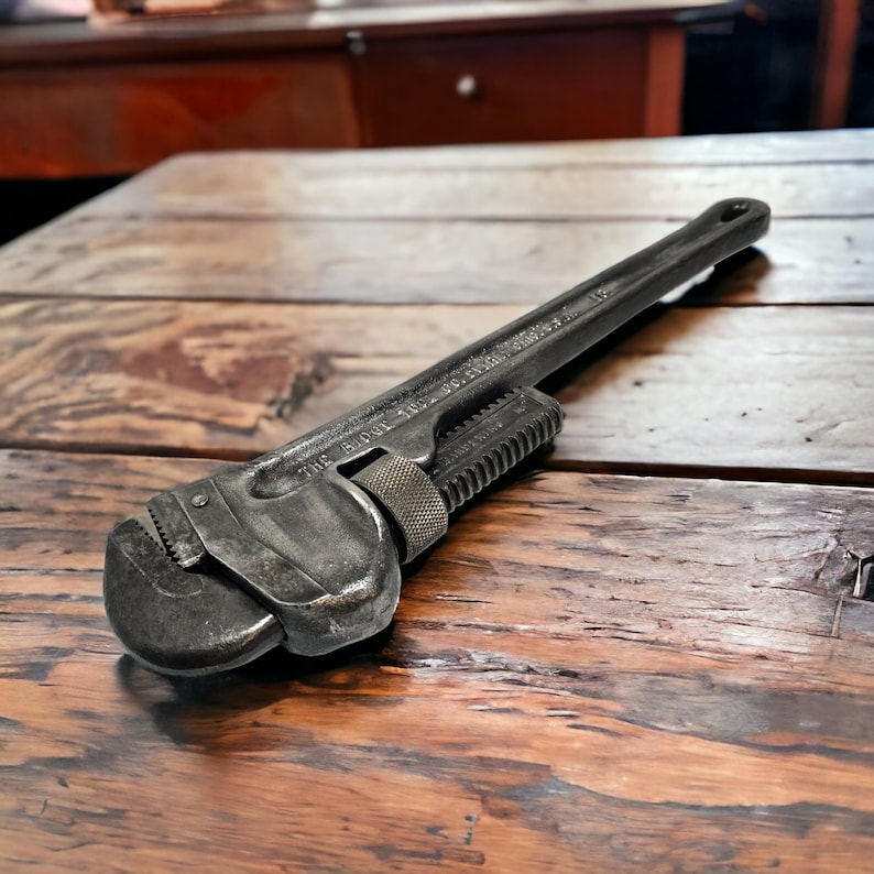 Puede incluir: Una llave inglesa ajustable vintage con acabado de metal negro. La llave est&aacute; sobre una superficie de madera.