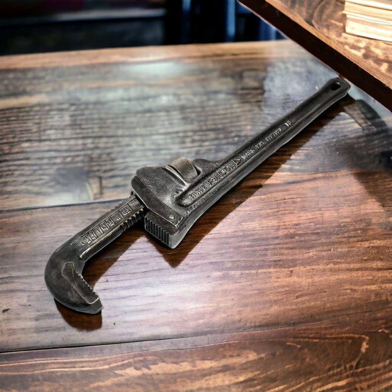 Puede incluir: Una llave inglesa negra con el texto "RIDGID  MADE IN U.S.A.  NO. 12" en el mango. La llave est&aacute; sobre una superficie de madera.