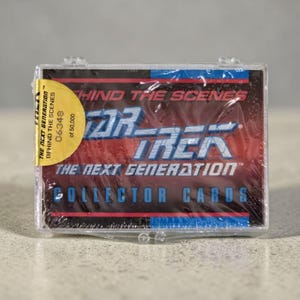 May include: A sealed plastic case containing a set of "Star Trek: The Next Generation" collector cards. The packaging features the show's logo and the text "Behind the Scenes." A round sticker indicates this is edition 06348 of 50,000.