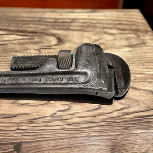Puede incluir: Una llave de tubo negra con el texto "THE RIDGE TOOL CO. ELMIRA, N.Y." en el mango.