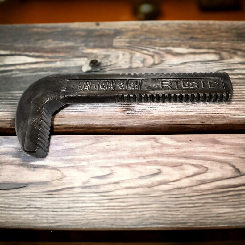Puede incluir: Una llave de tubo negra con la palabra "RIDGID" impresa en el mango. La llave tiene una mand&iacute;bula dentada y una escala marcada en pulgadas.