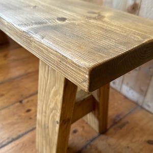 May include: A rustic wooden bench with a natural wood finish. The bench has a simple A-frame design and is made from solid wood.