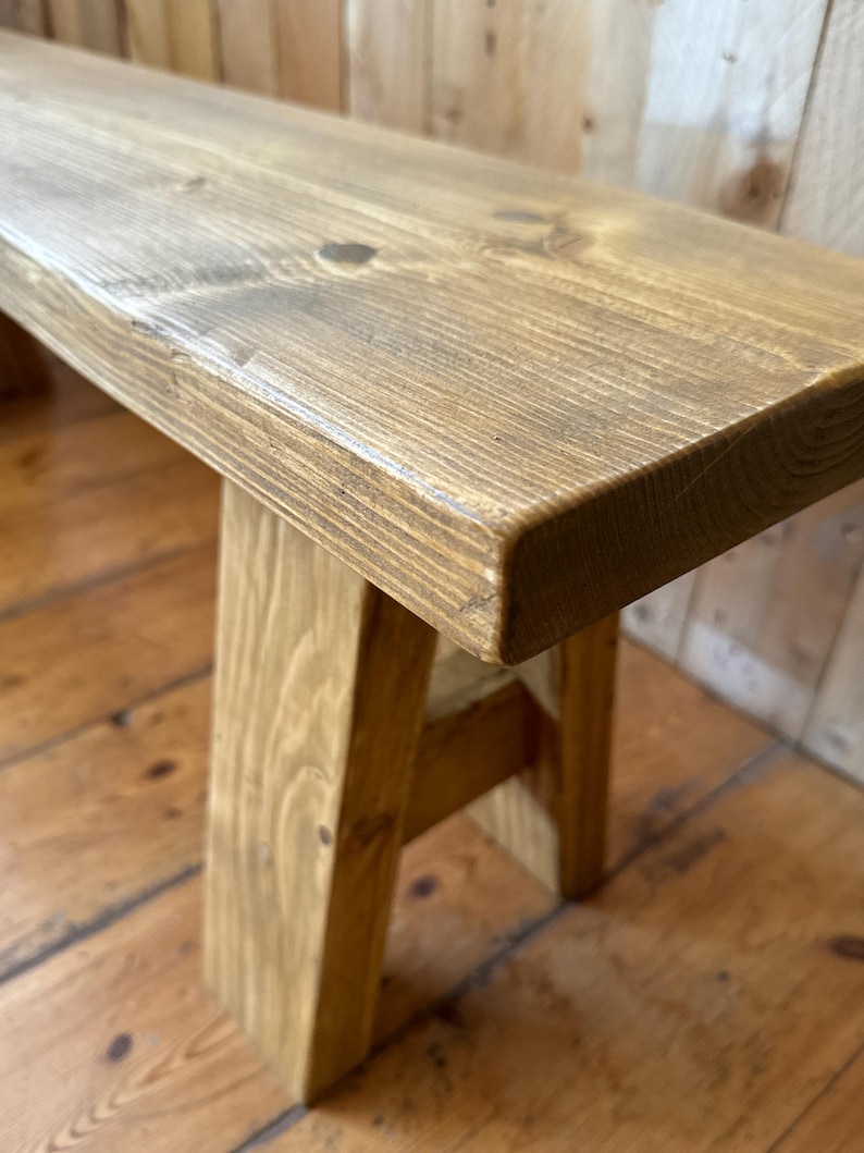 May include: A rustic wooden bench with a natural wood finish. The bench has a simple A-frame design and is made from solid wood.