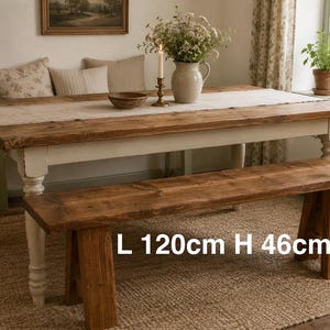 May include: A wooden dining table and bench set. The table is 120cm long and the bench is 46cm high. The table has a white base and a natural wood top. A beige runner and floral arrangement are on the table, creating a rustic feel.