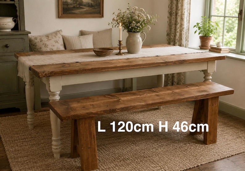 May include: A wooden dining table and bench set. The table is 120cm long and the bench is 46cm high. The table has a white base and a natural wood top. A beige runner and floral arrangement are on the table, creating a rustic feel.