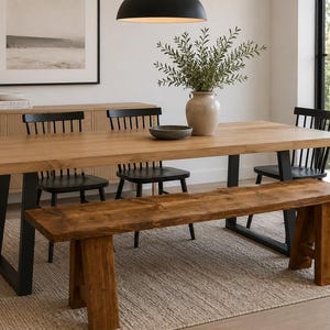 May include: A light wood dining table with black metal legs, surrounded by black chairs and a wooden bench. A beige rug and a vase with greenery complete the dining room setting. The table is approximately 244 cm long.
