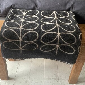 May include: A black and white patterned throw blanket with a simple leaf design is draped over a wooden bench.