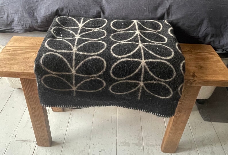 May include: A black and white patterned throw blanket with a simple leaf design is draped over a wooden bench.