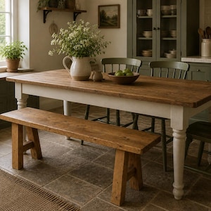 May include: A rustic wooden dining table with a white base and a matching bench. The table is topped with a brown surface and is surrounded by green chairs. A white pitcher with flowers sits on the table.