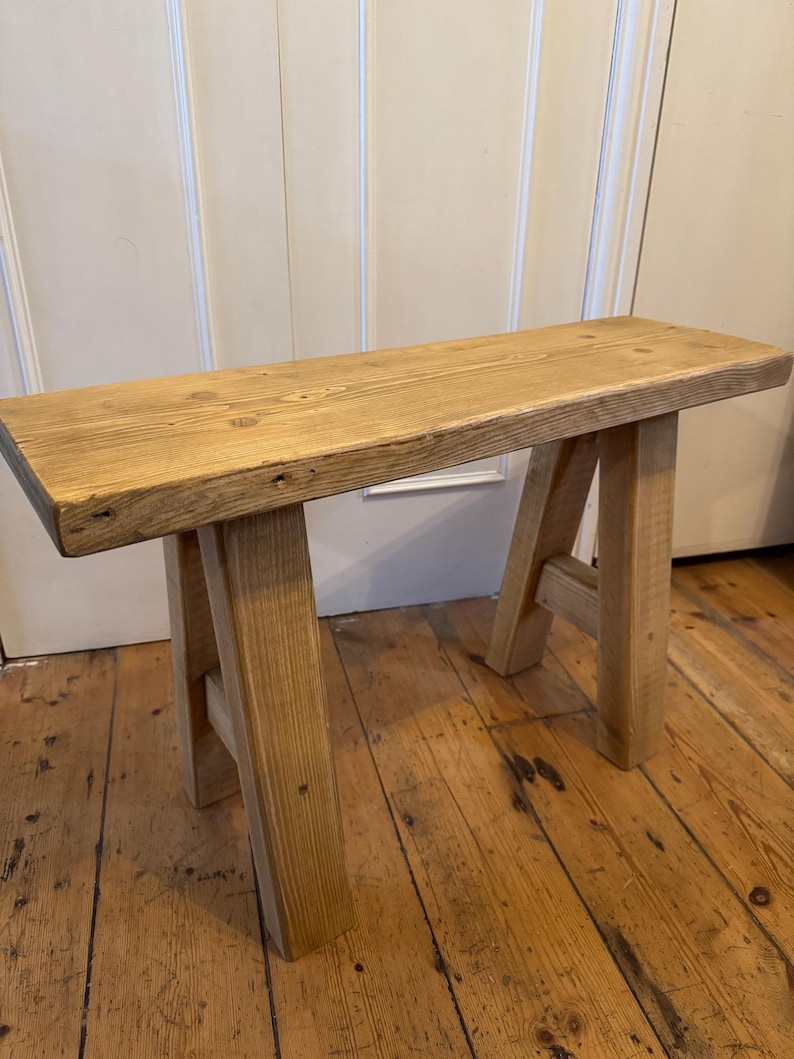 May include: A small, natural wood bench with a rectangular seat and A-frame legs. The bench is made of light-colored wood with visible grain and knots. The bench is approximately 36 inches long.