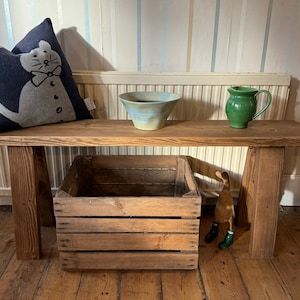May include: A rustic wooden bench with a wooden crate, a green ceramic jug, and a blue and white ceramic bowl. The bench is against a striped wall.