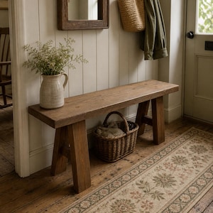 May include: A wooden bench with a natural finish in a hallway setting. A woven basket is placed beneath the bench, and a floral runner rug leads towards a door. A vase with greenery and a mirror are also visible.