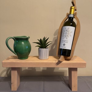 May include: A wooden wine bottle holder shaped like a bird with a green pitcher and a potted succulent plant on a wooden bench.
